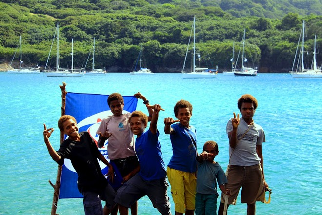 WCC - Tanna in Vanuatu - Kids on rocks with flag and rally yachts in the background © Jeremy Wyatt
